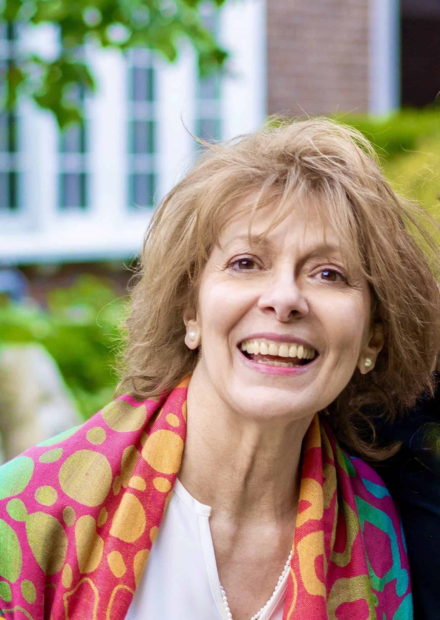 Elegant woman smiling outdoors, wearing a colorful scarf at a joyful Odyssey Events gathering.