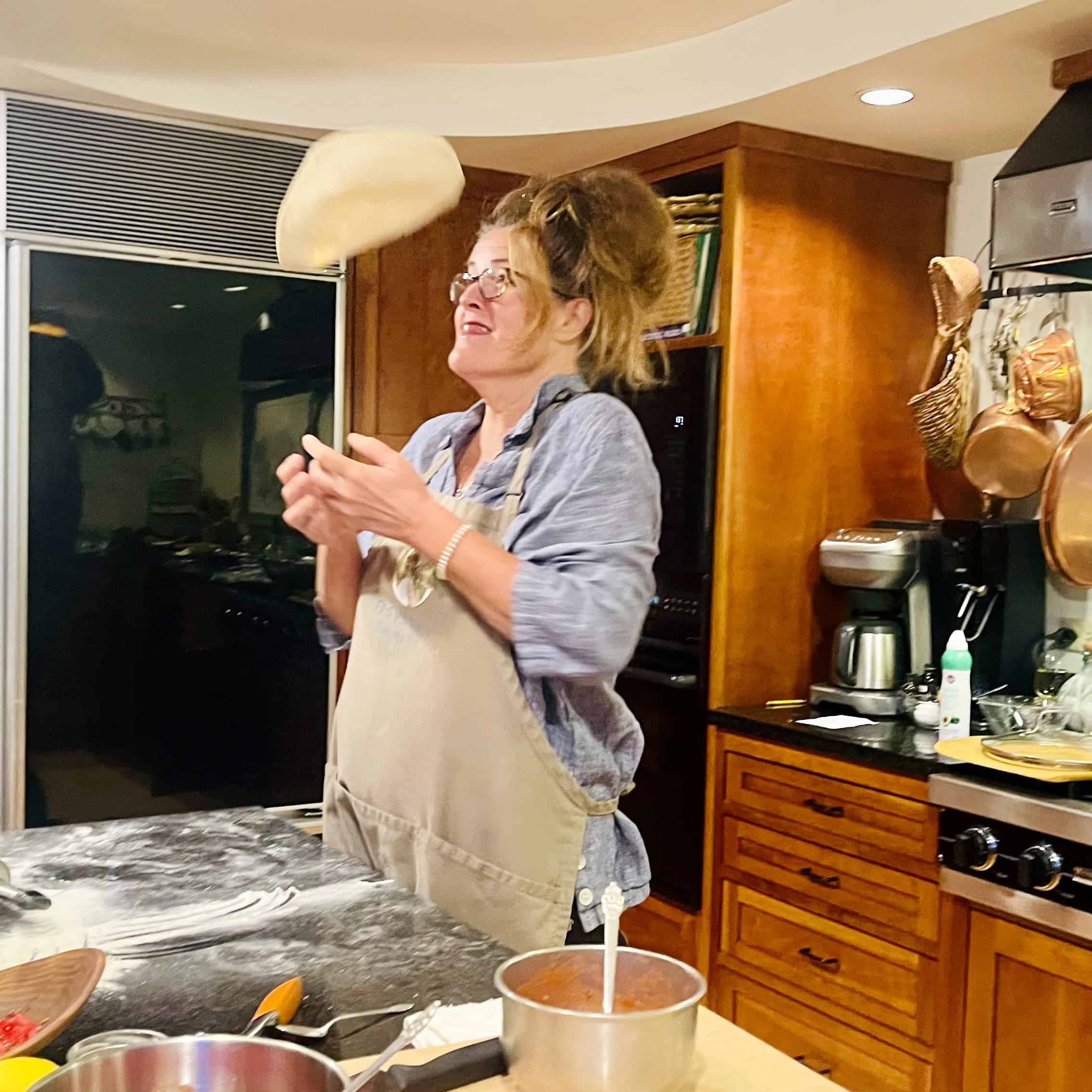 Woman tossing pizza dough in a cozy kitchen setting.