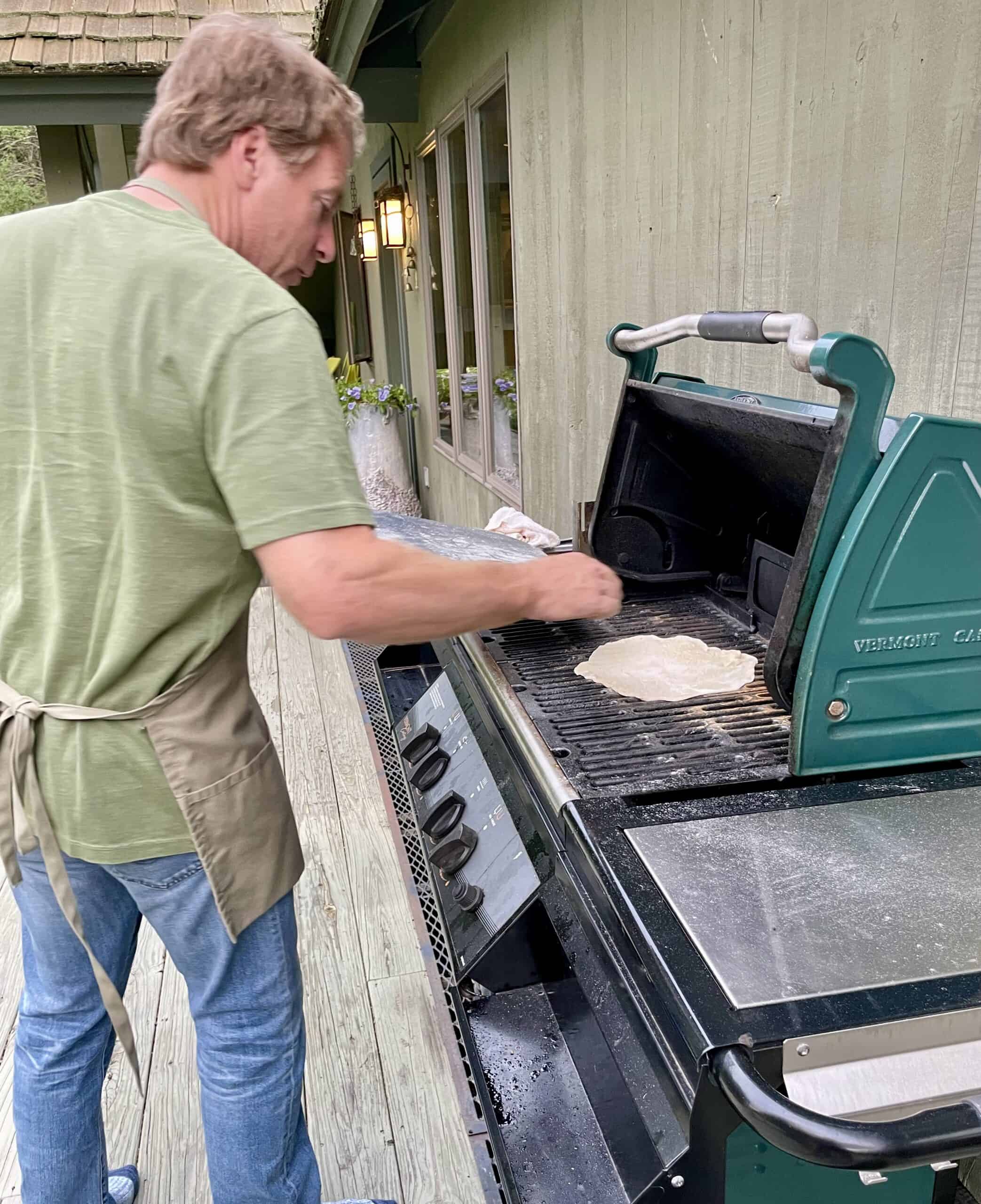 Outdoor pizza chef making fresh pizza on a grill for a celebration.