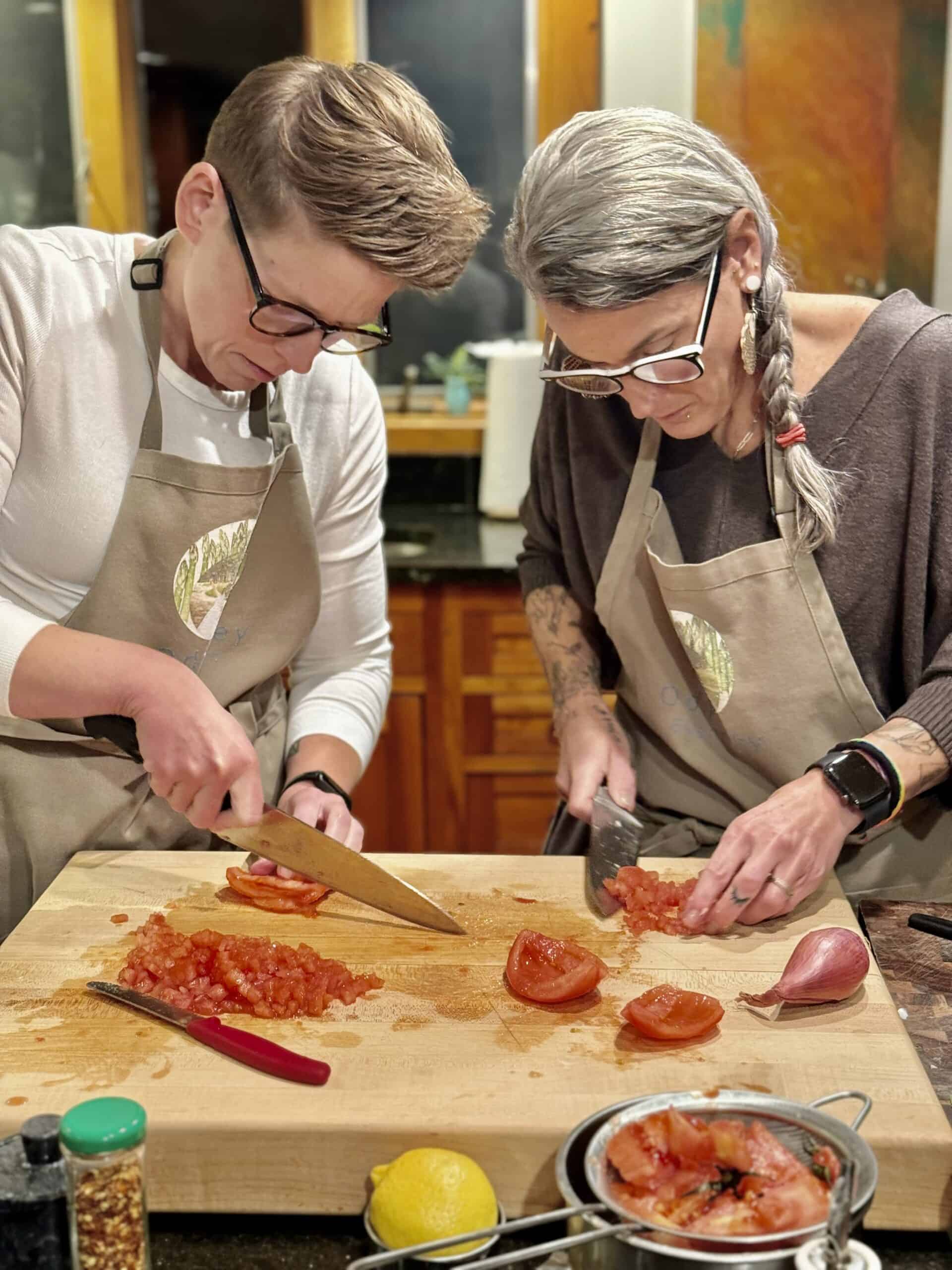 Cooking class with two women chopping tomatoes and onions in a kitchen.