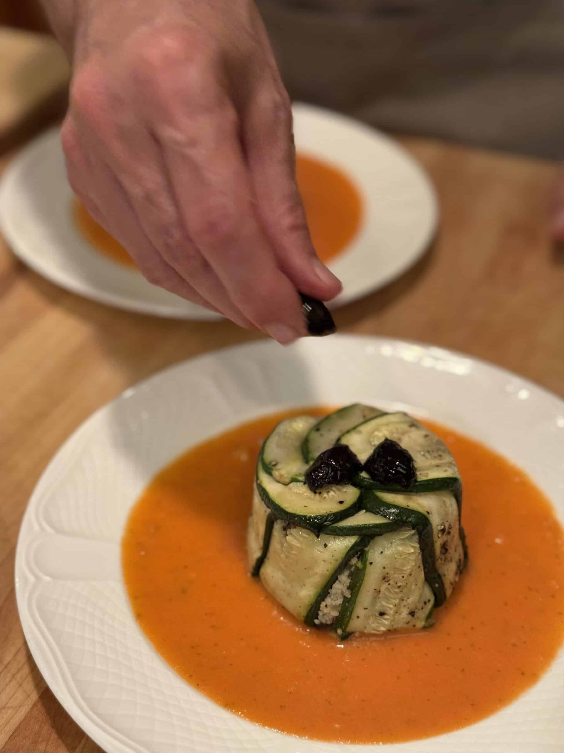 Elegant plated dish with zucchini and black olives, served with a vibrant orange sauce.