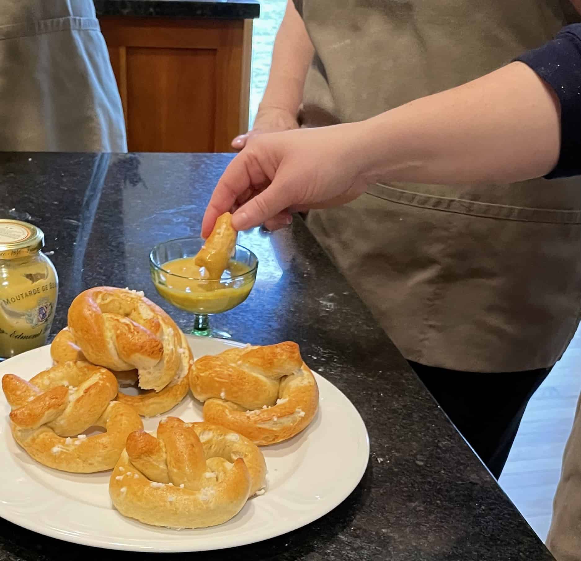 Hand dipping pretzel into mustard sauce on a black countertop.
