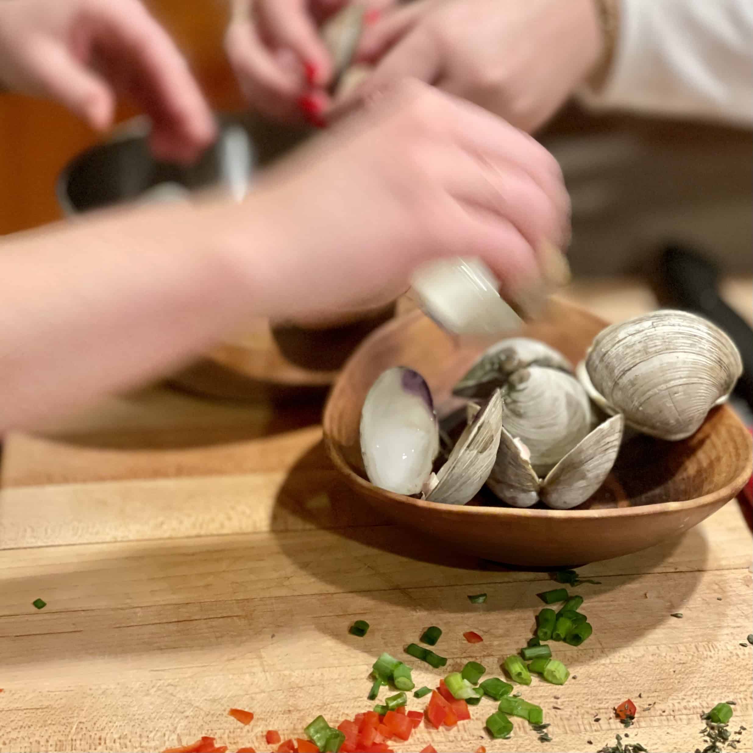 Fresh clams and chopped vegetables on a wooden table for a seafood dish.