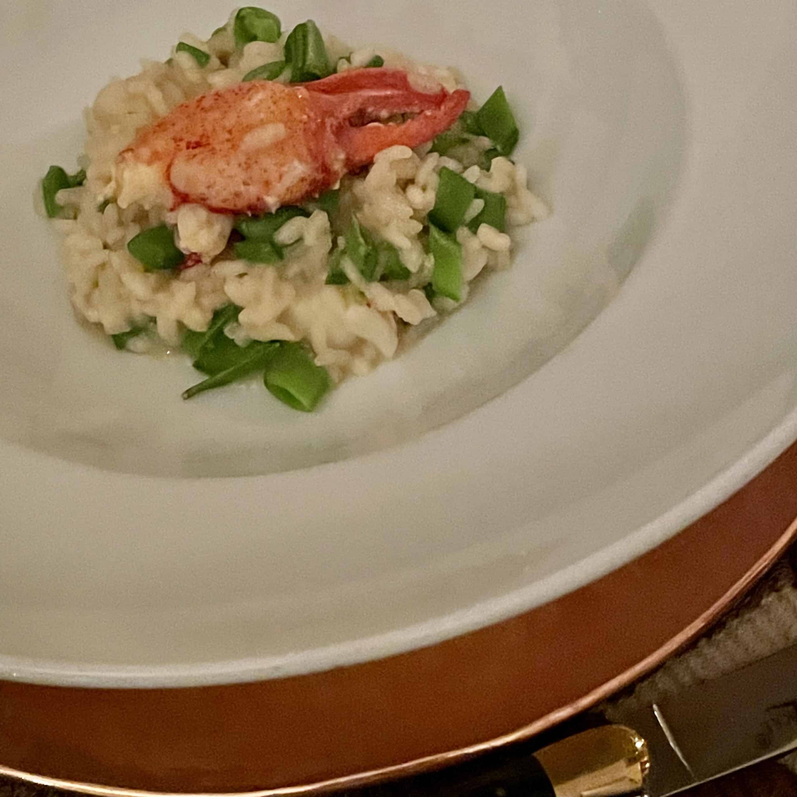 Lobster risotto garnished with chopped green onions served on a white plate.