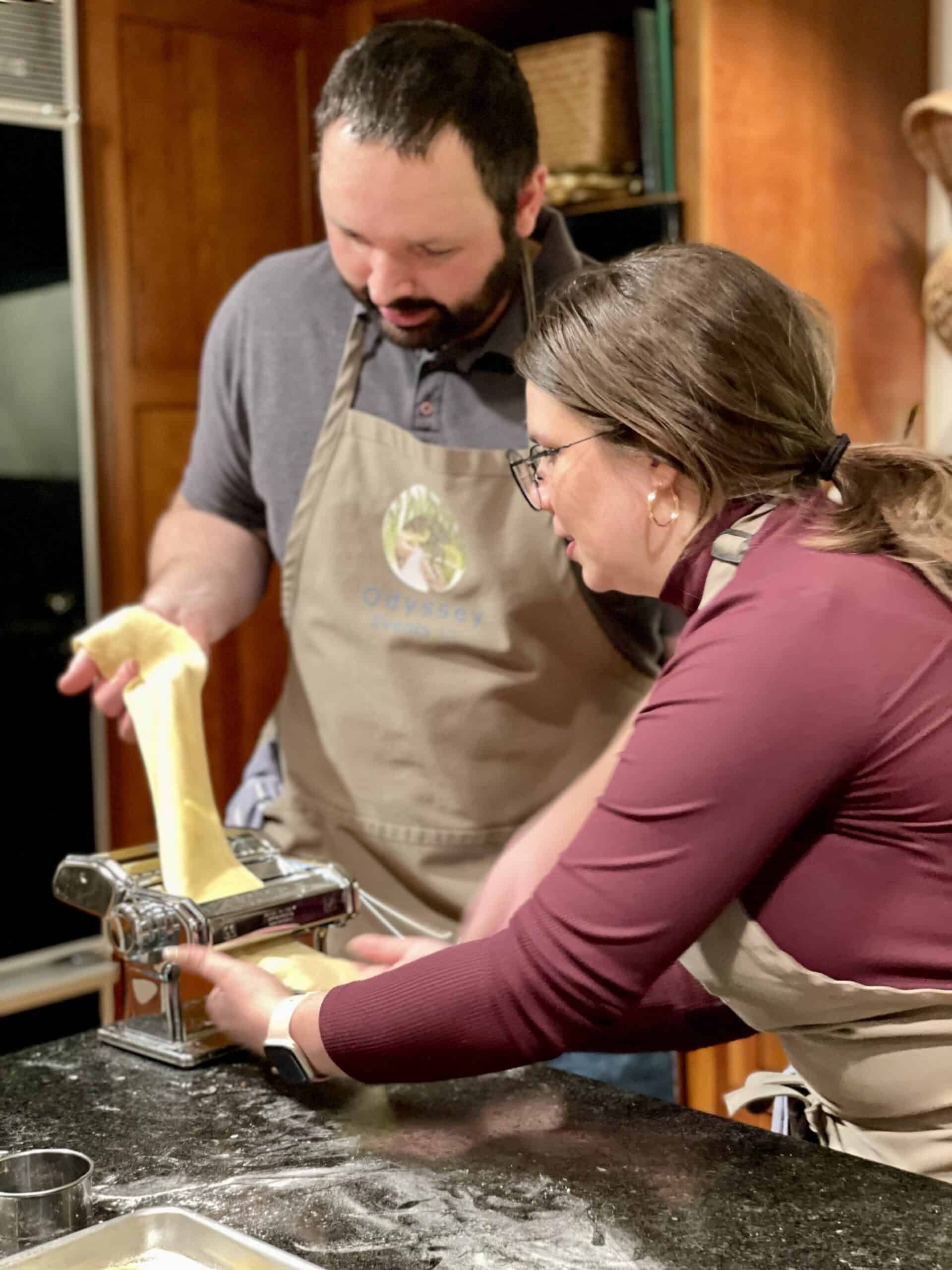 Two people making fresh pasta with a pasta machine in a cozy kitchen.