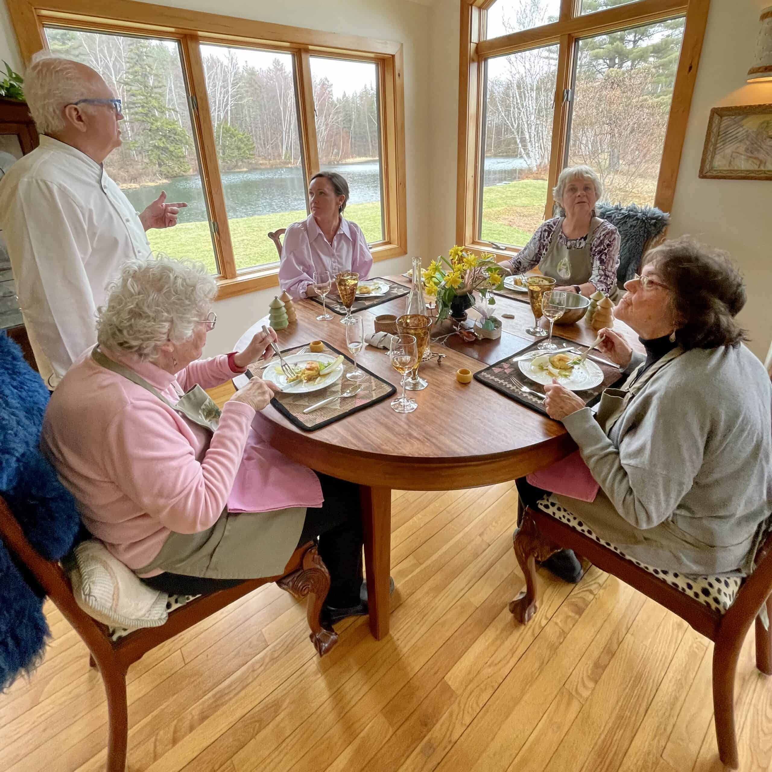 Senior women dining together at a round table in a bright, scenic room.