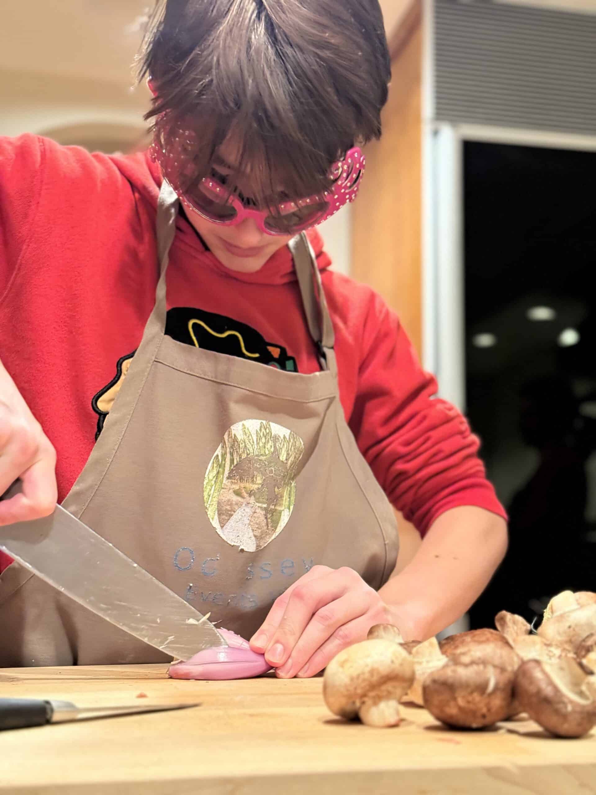 Kids cooking class with a young child chopping mushrooms, promoting fun and educational culinary act.