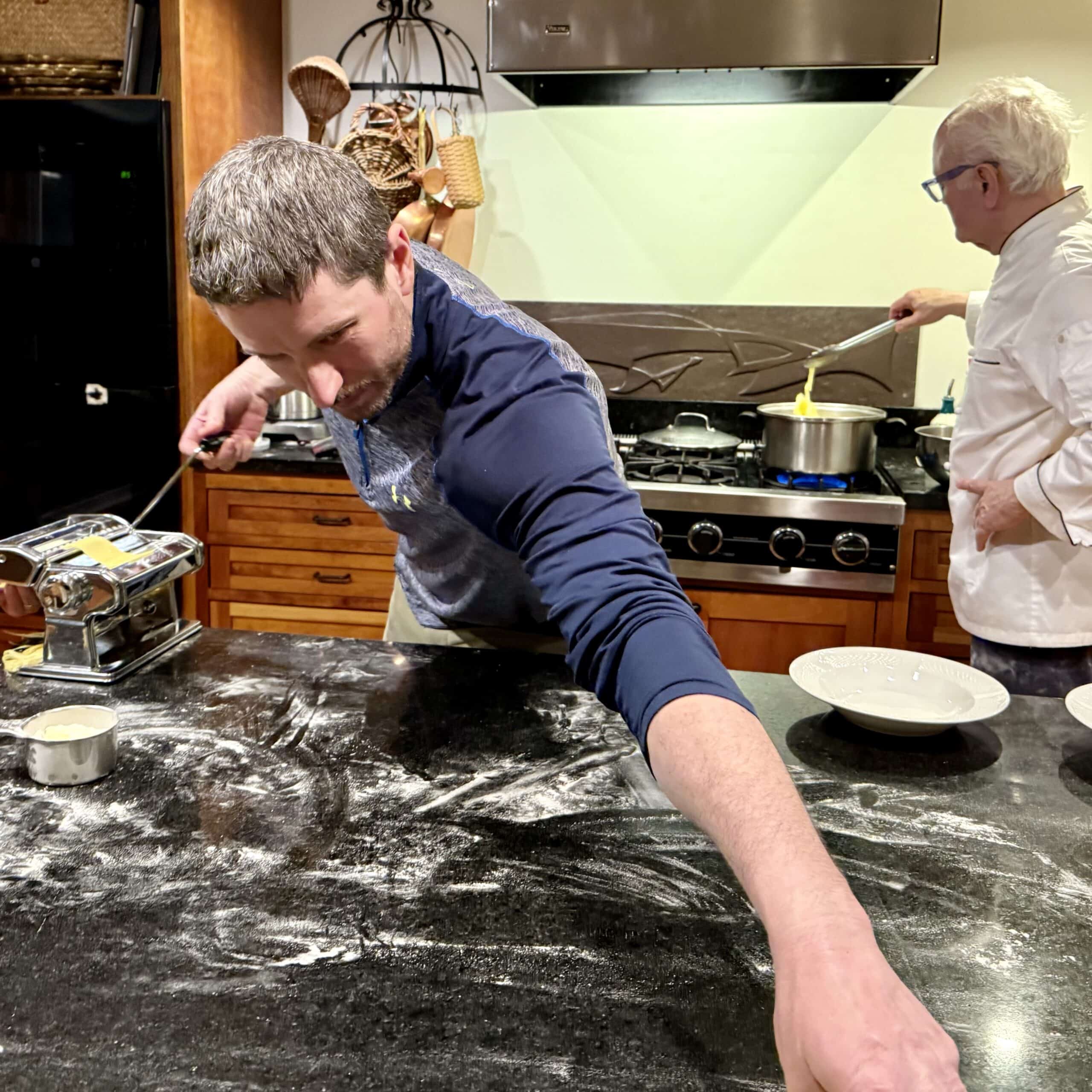 Chef preparing pasta while another chef stirs sauce on stove.