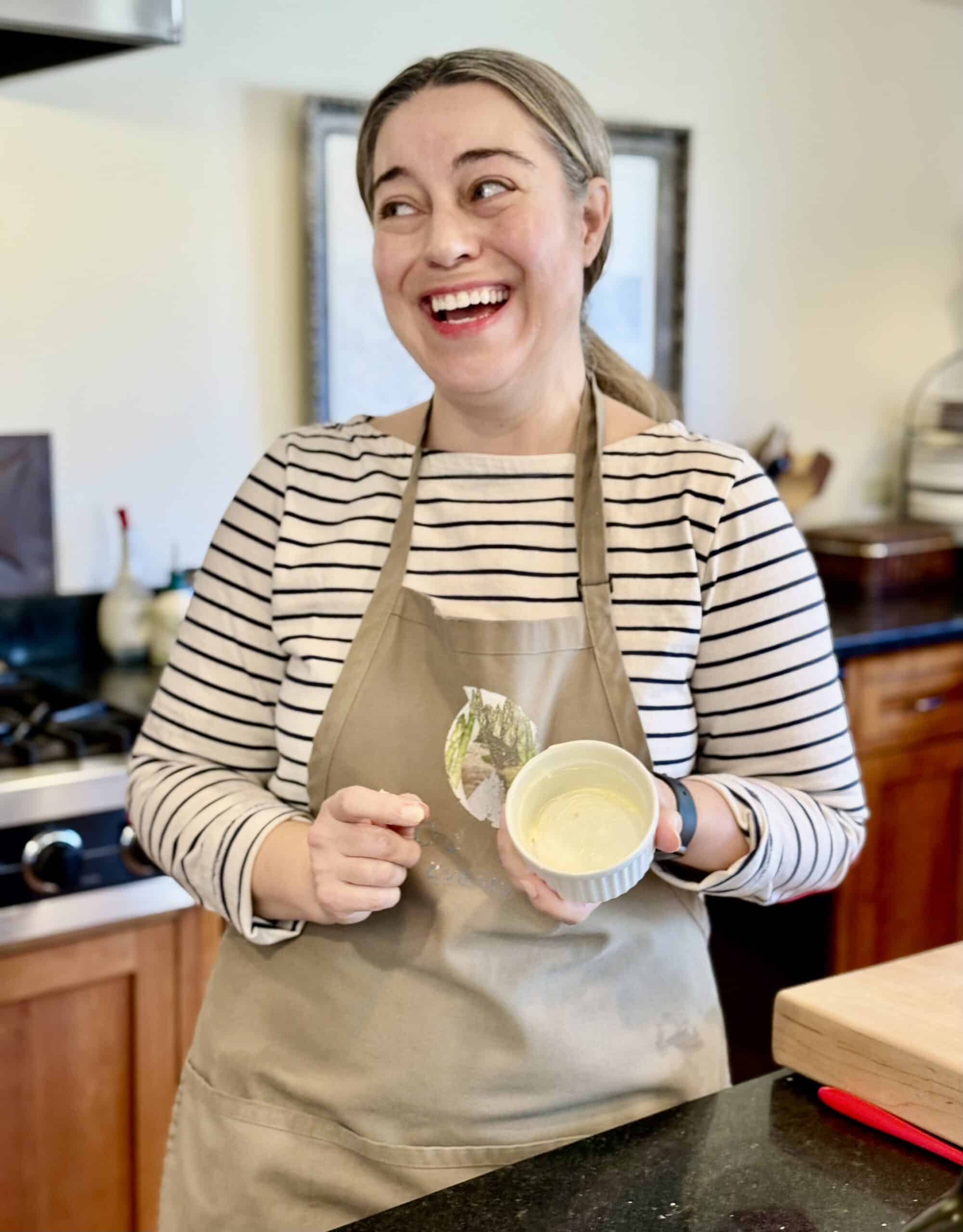 Woman smiling in kitchen holding a bowl of batter, preparing for a cooking event.