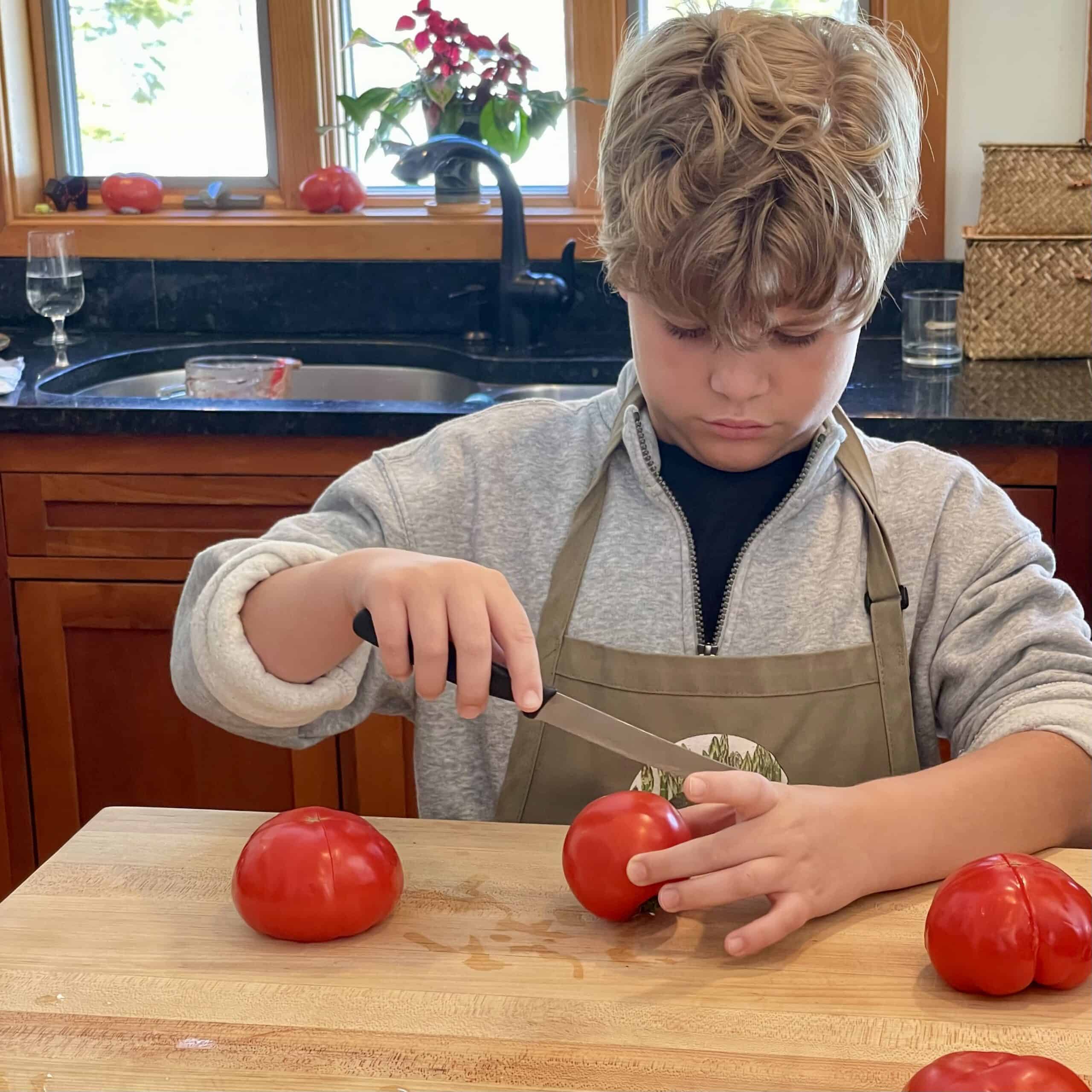 Child slicing tomatoes on a wooden cutting board in a cozy kitchen.