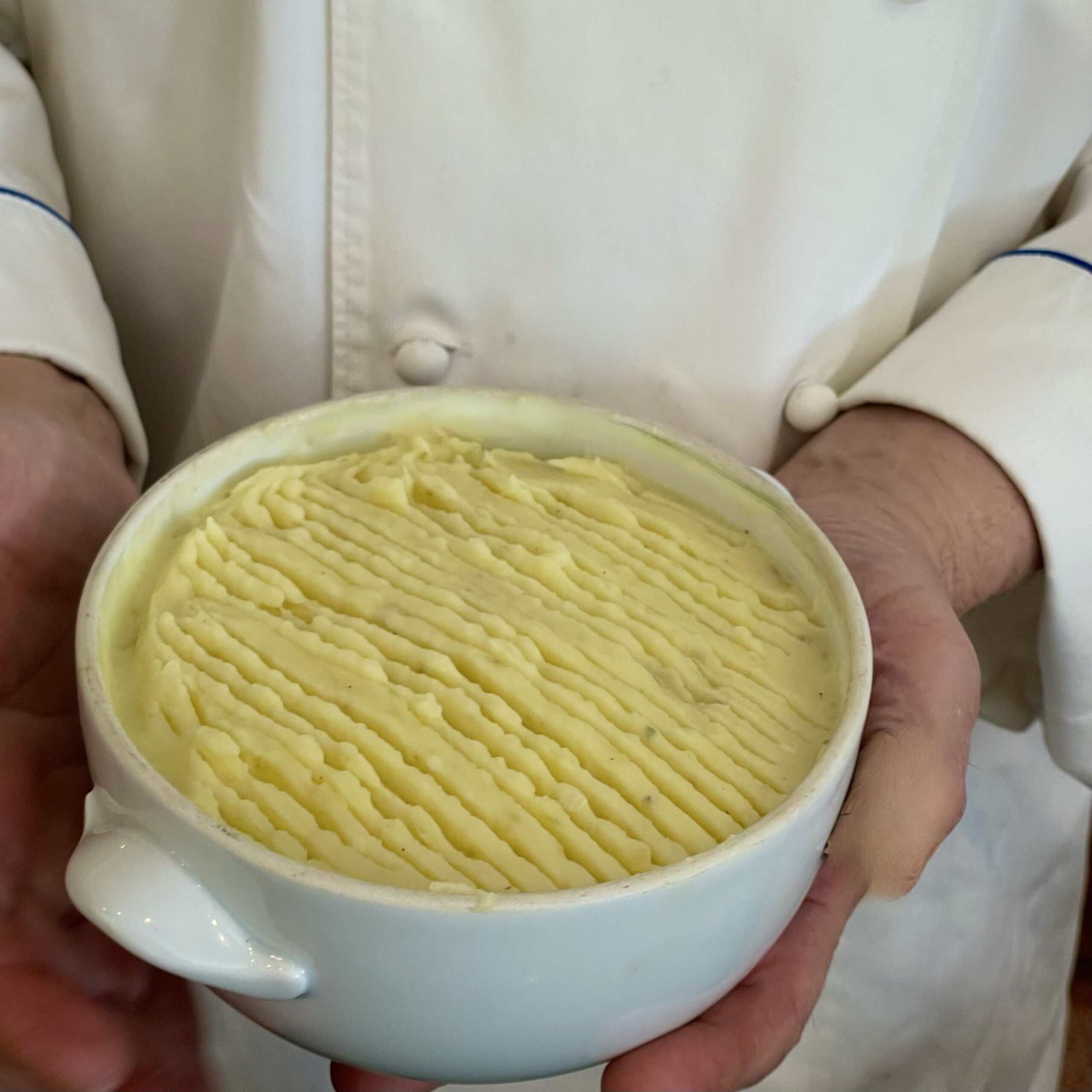 Chef holding a bowl of creamy mashed potatoes, ready for serving.