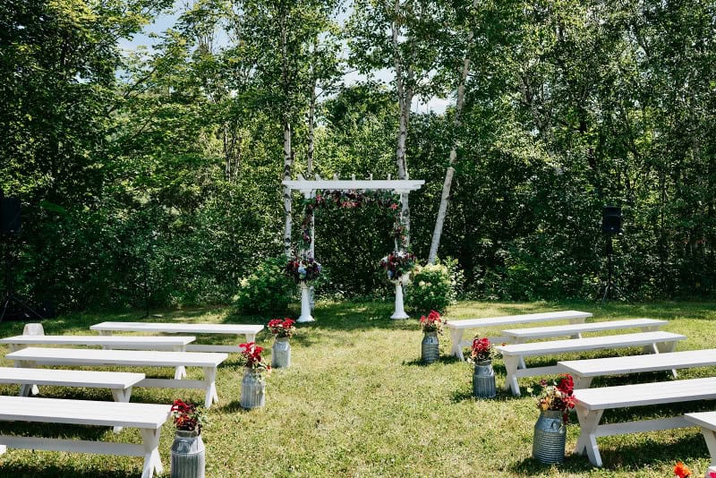 Elegant outdoor wedding ceremony with floral arrangements and white benches.