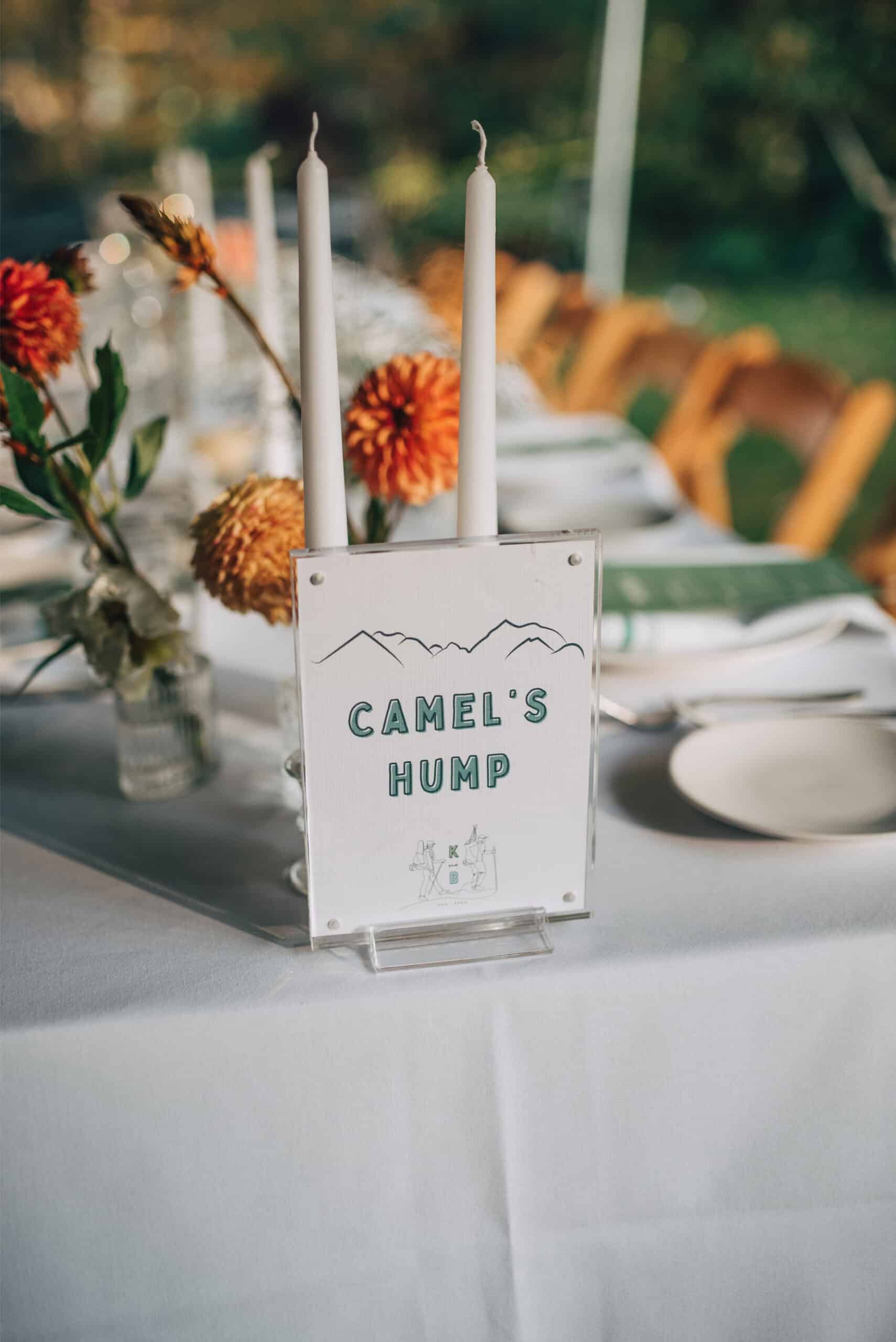 Outdoor event table with floral arrangements, candles, and a "Camel's Hump" sign.