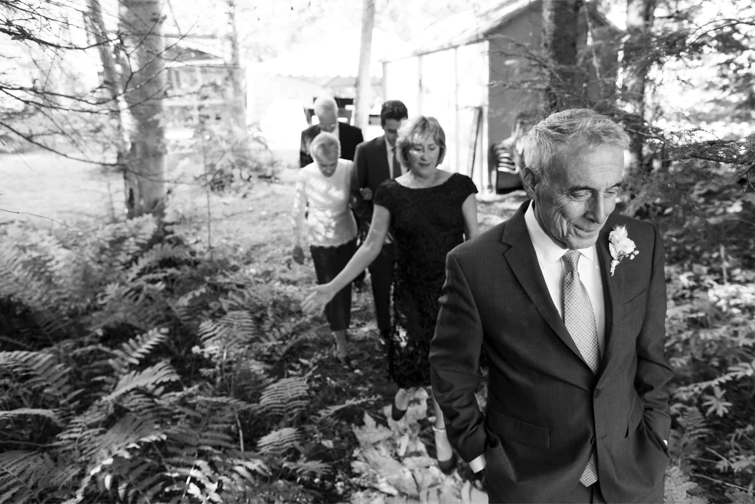 Elegant outdoor wedding ceremony with guests walking through lush greenery.
