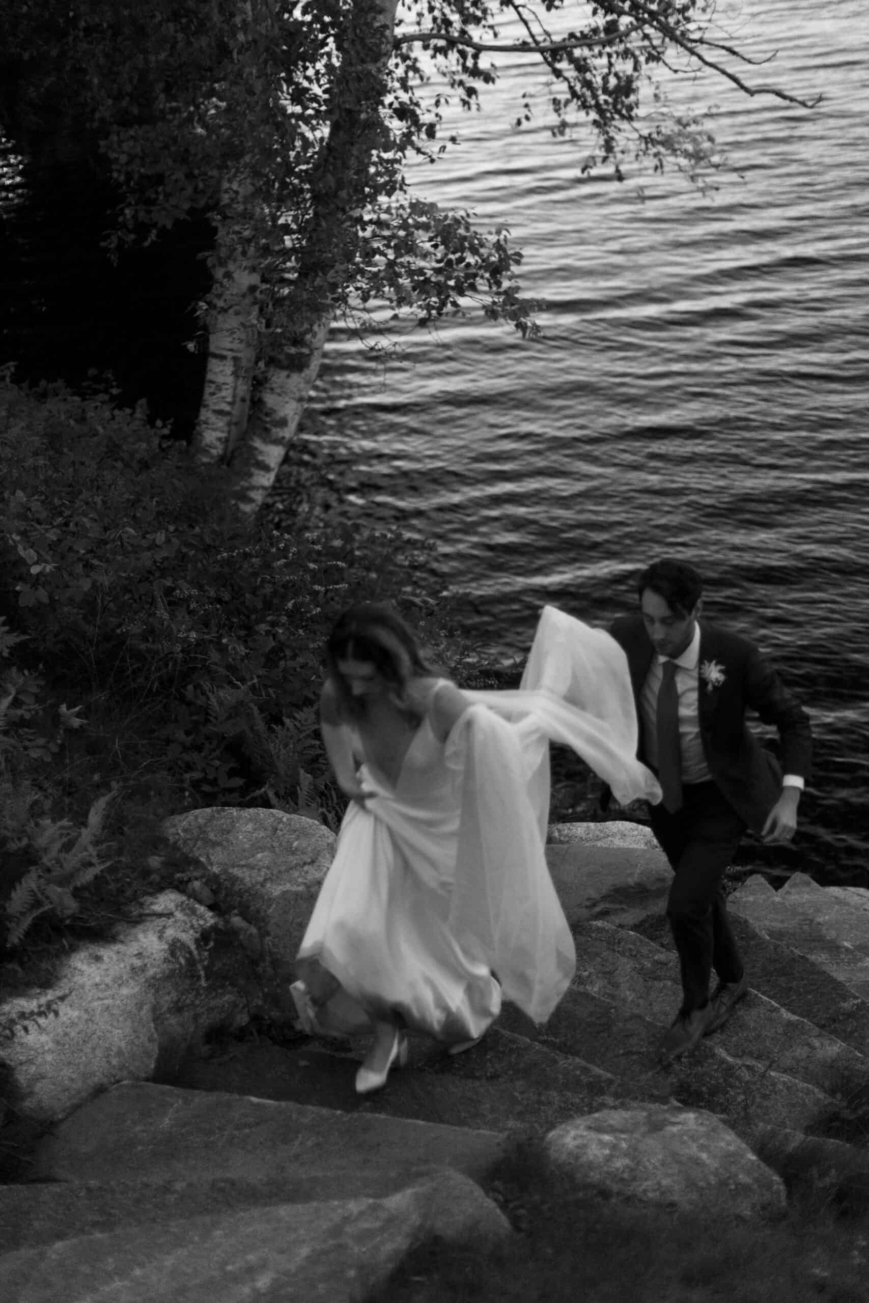 Wedding couple walking up stone steps near water, outdoor wedding scene.