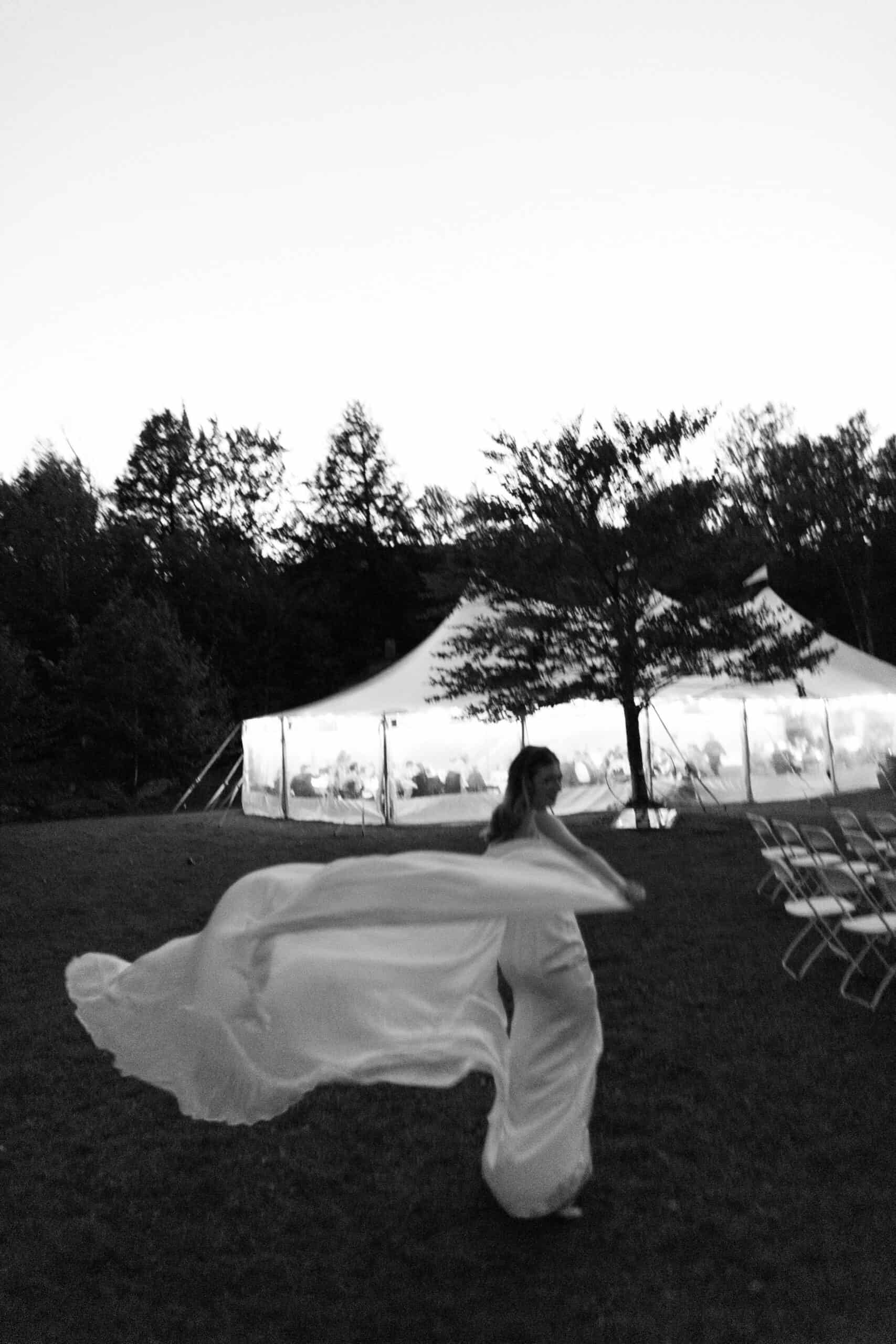 Bride dancing outdoors at wedding reception with tent and trees in background.
