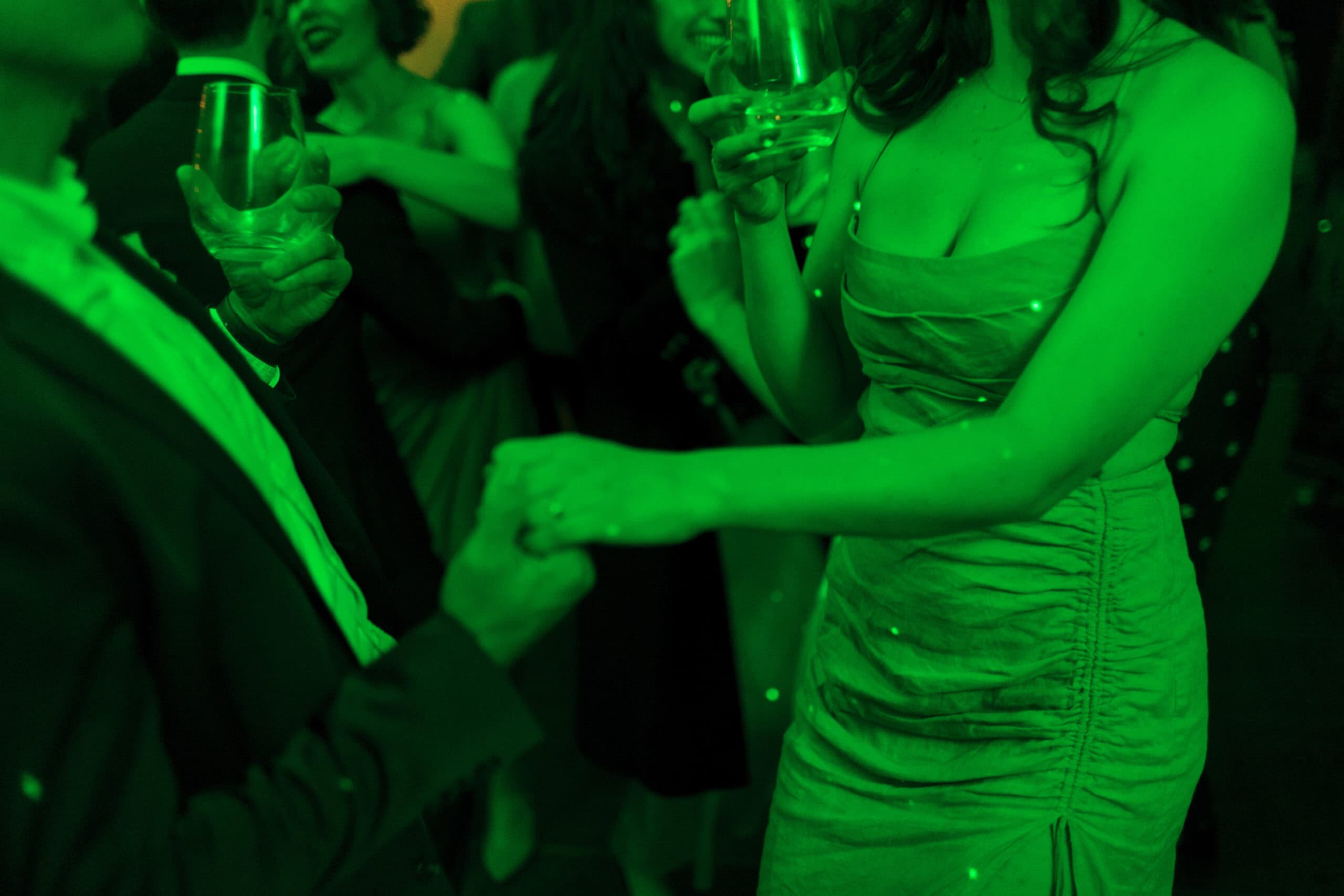 Elegant couple dancing at a lively event with guests holding drinks.