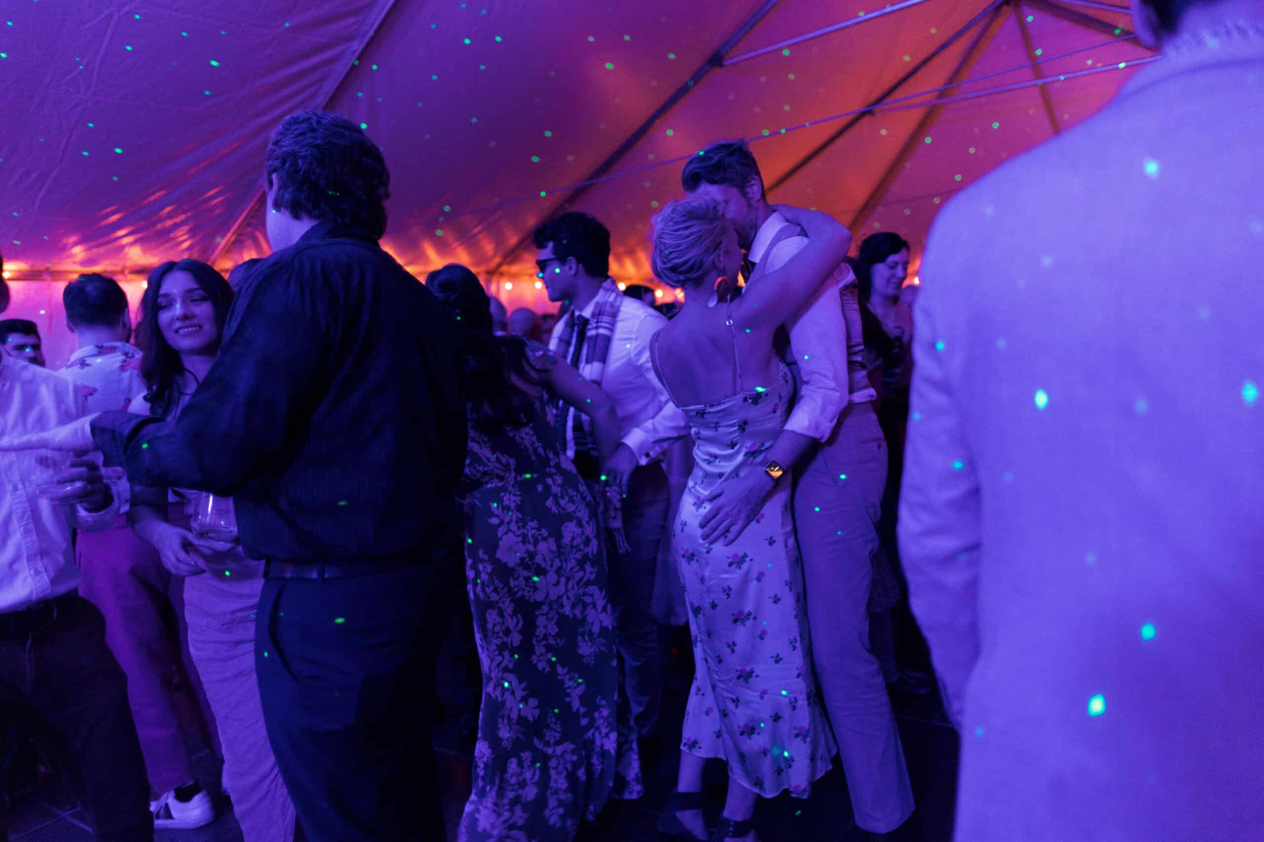 Dancing guests at Odyssey Events under colorful lighting and a vibrant tent ceiling.