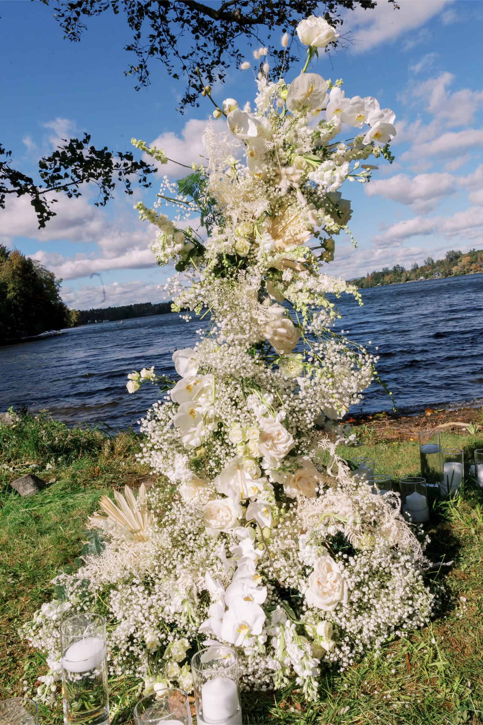 White floral arch with roses and baby's breath by the water.