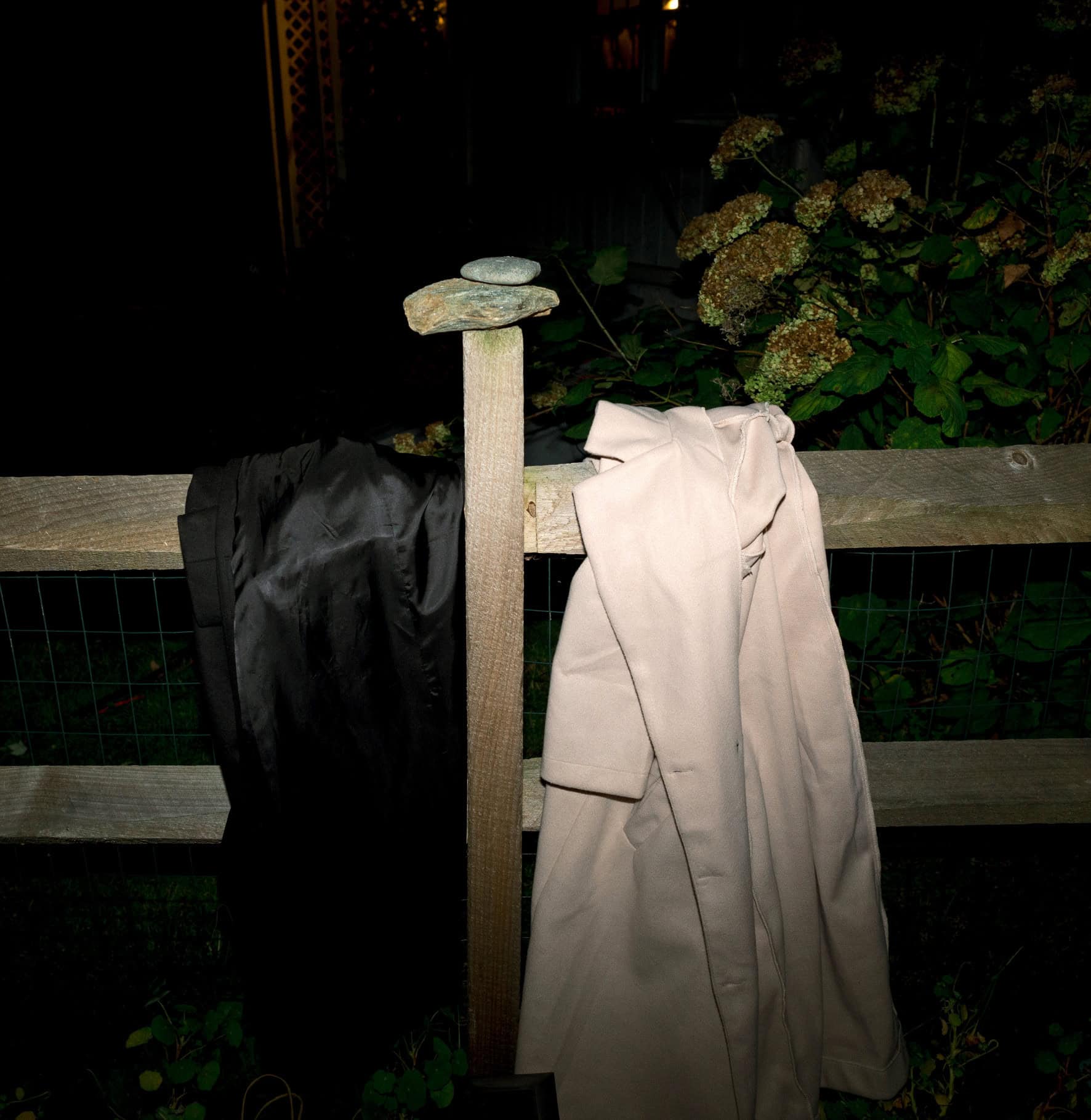 Black and beige coats hanging on a wooden fence with decorative stones on top.
