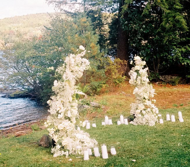 Wedding floral arch with white flowers and candles near a lake.