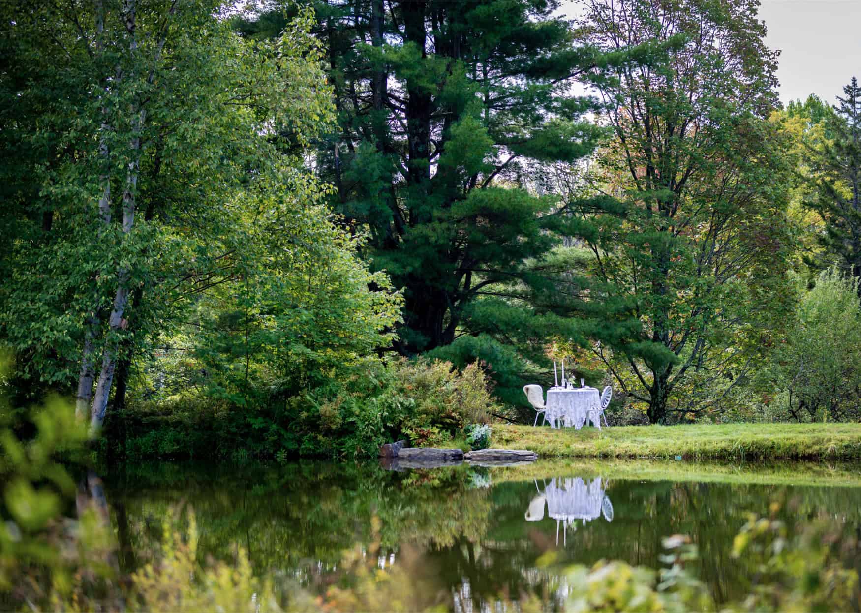 Outdoor lake event with lush trees and a decorated table for special occasions.