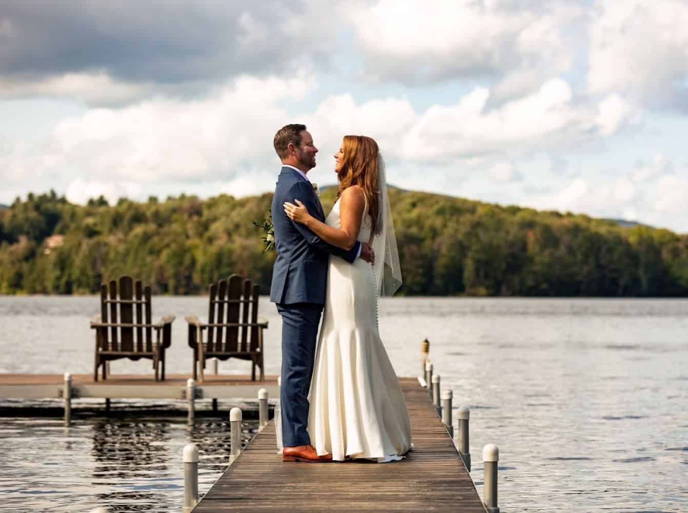 Wedding couple embracing on lakeside dock, scenic outdoor setting for special event.