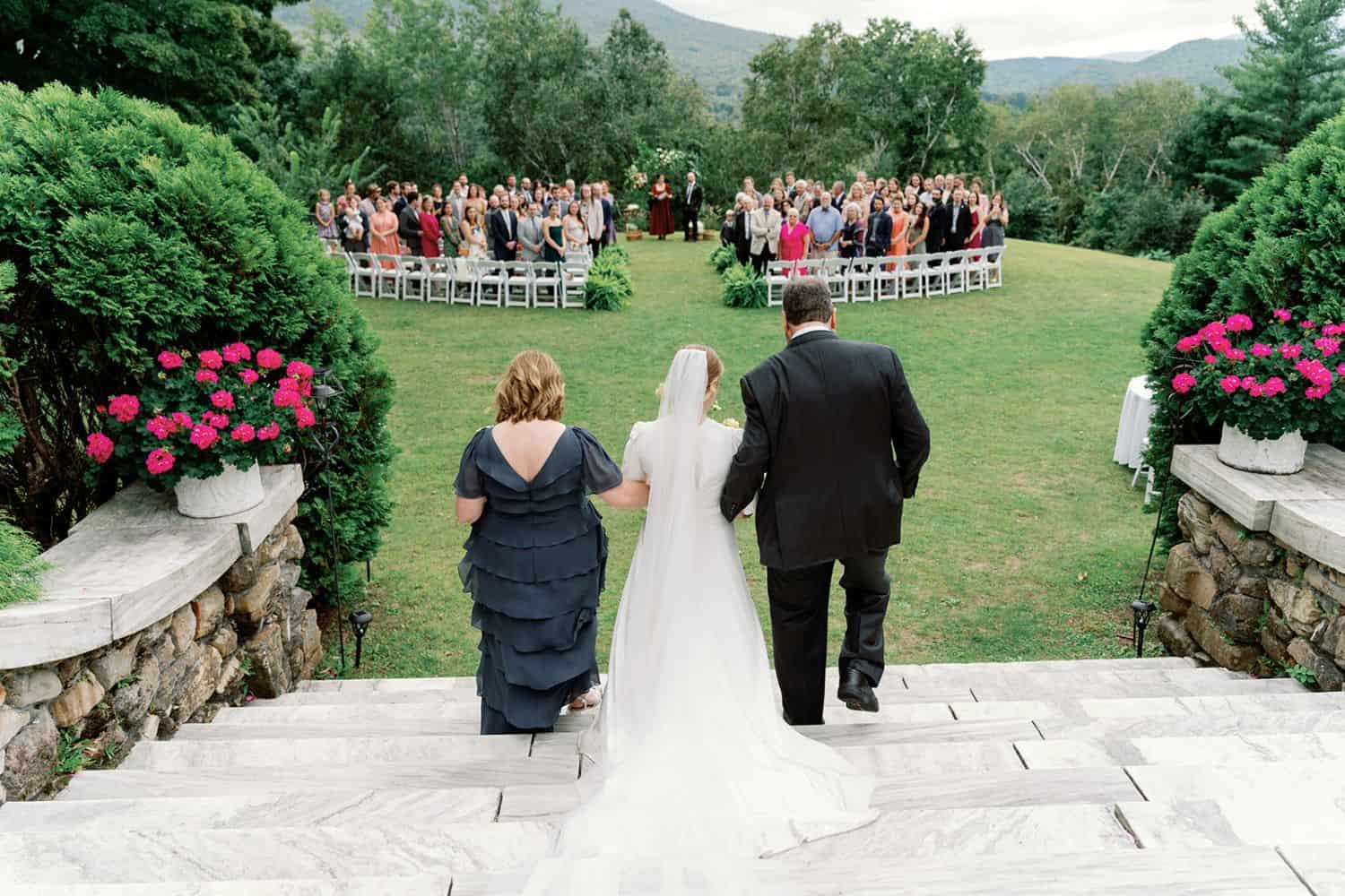 Outdoor wedding ceremony with bride, groom, and guests in scenic garden setting.