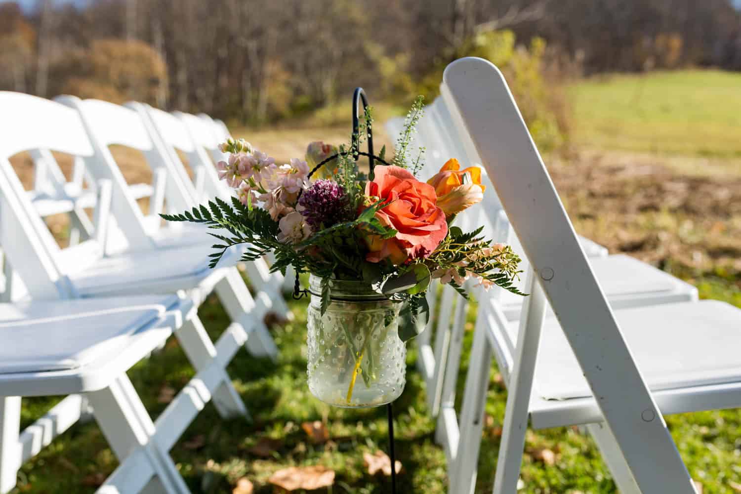 Beautiful flower bouquet hanging on white chairs at an outdoor wedding venue.