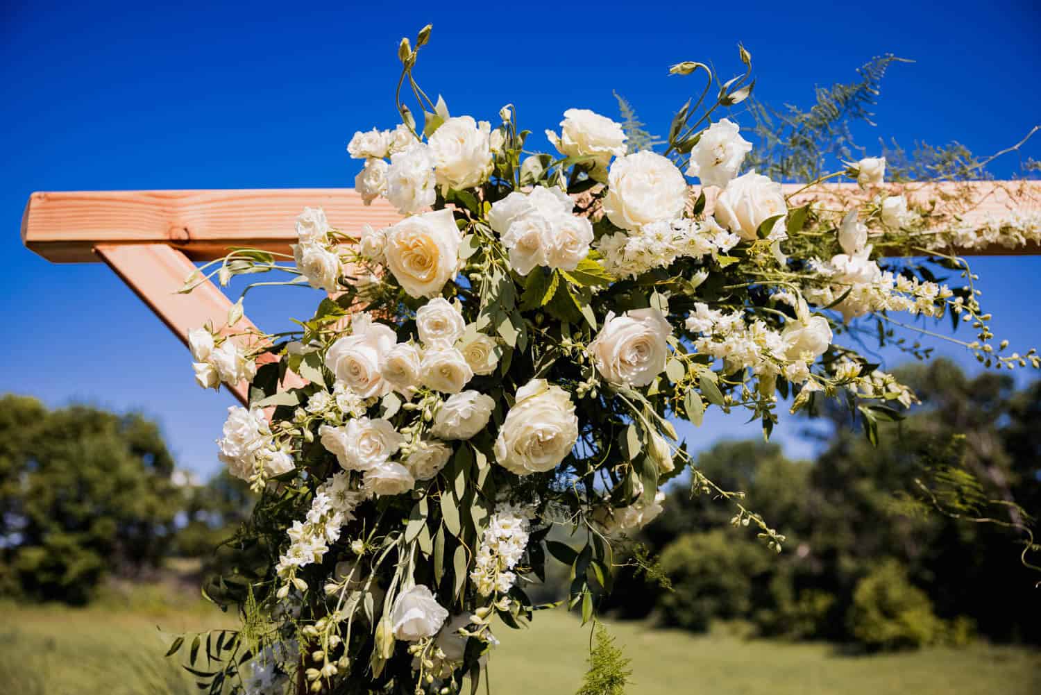 Elegant wedding floral arch with white roses and greenery for outdoor ceremonies.