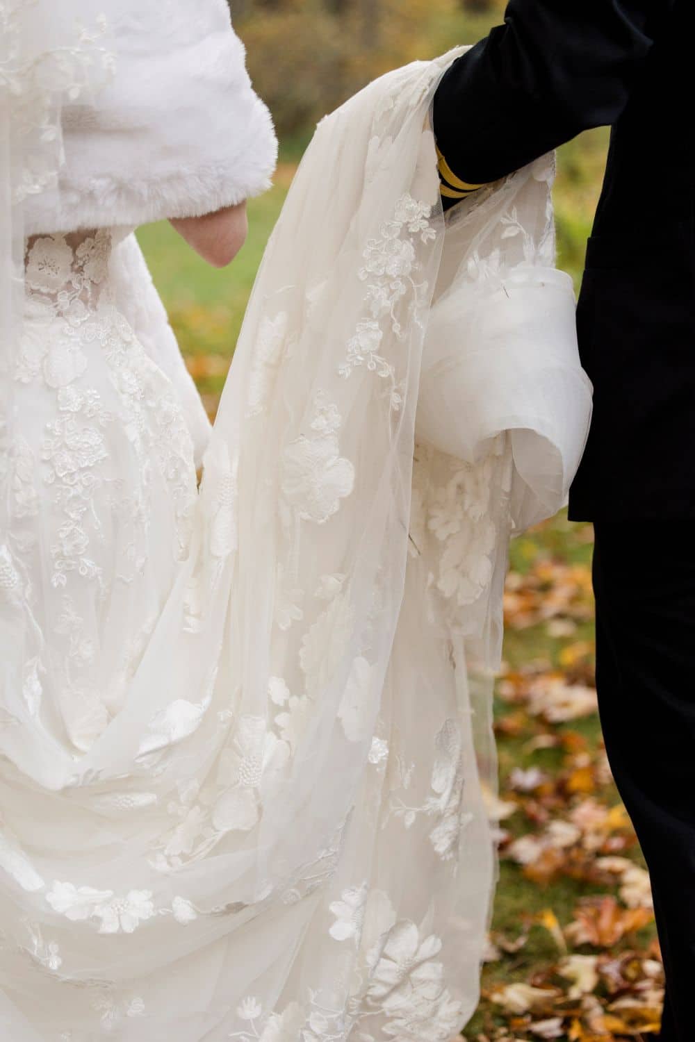 Elegant wedding couple holding lace wedding dress outdoors in autumn leaves.