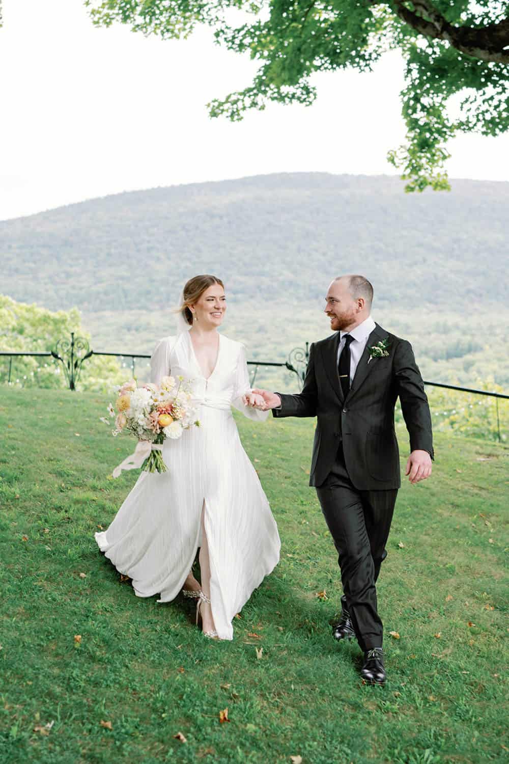 Bride and groom walking hand in hand in a scenic outdoor setting.