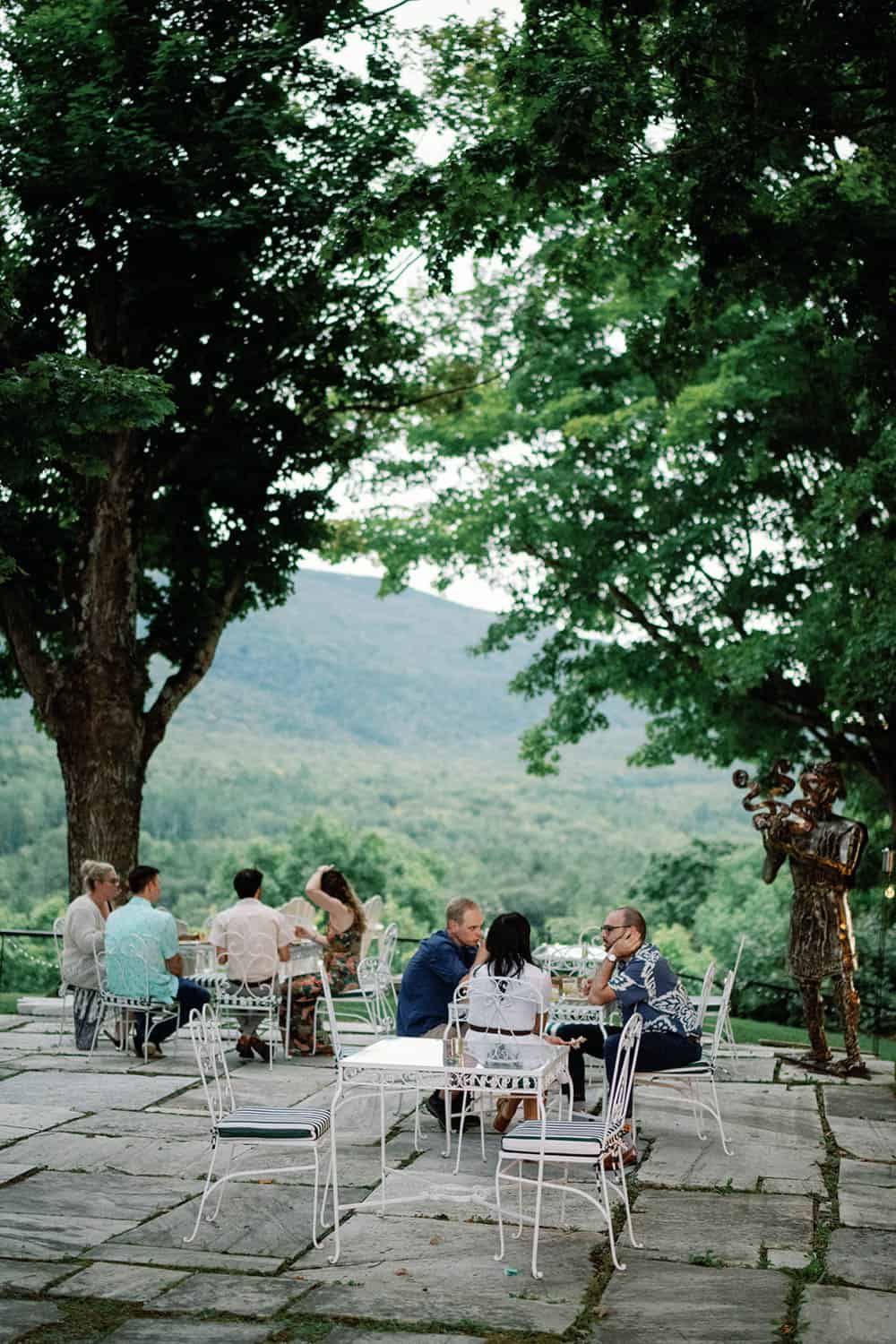 Outdoor event setup with guests enjoying a gathering beneath large trees.