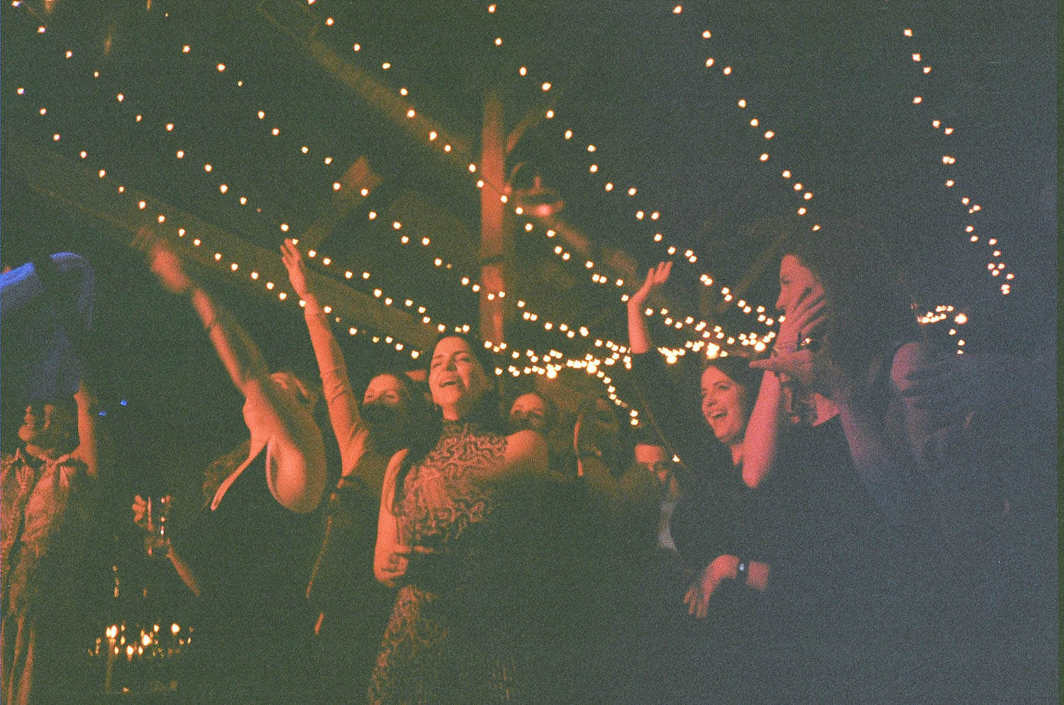 People dancing and enjoying a celebration under string lights.