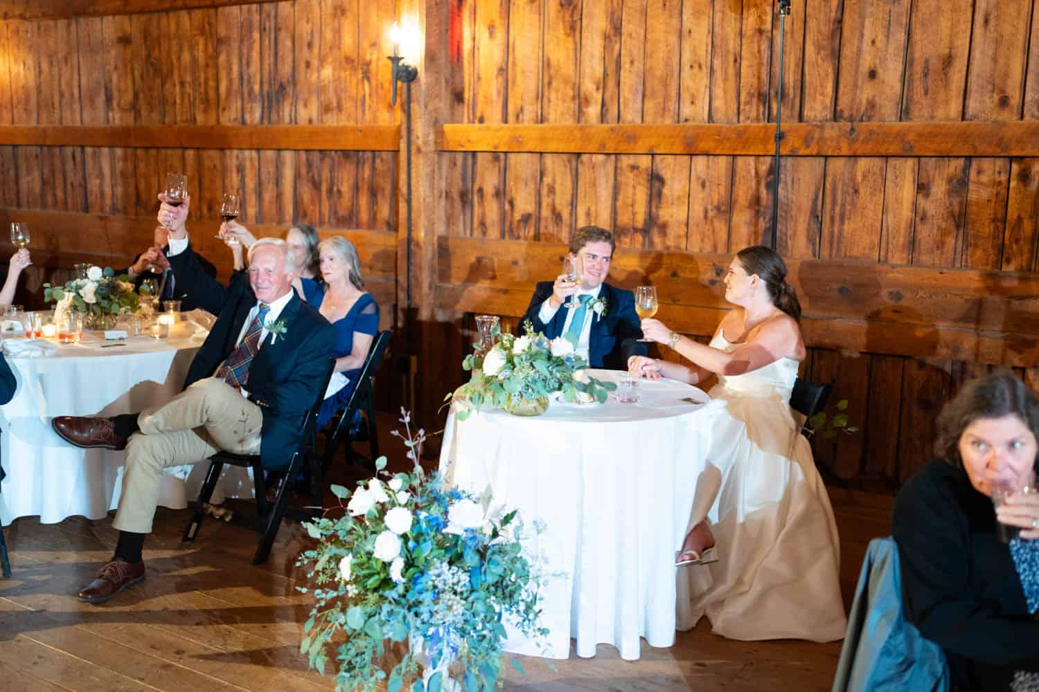 Wedding reception with guests raising glasses in a rustic wooden barn setting.