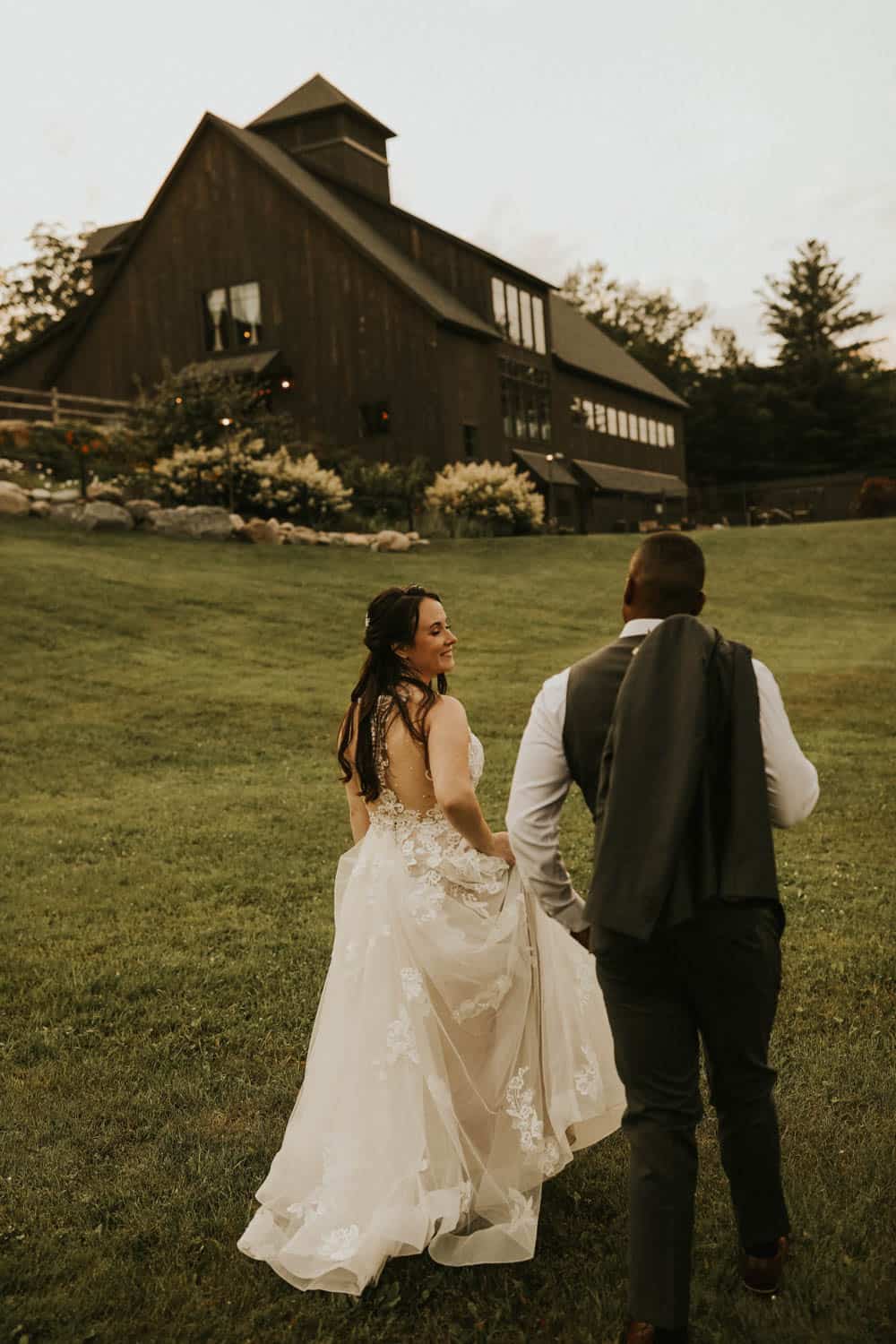 Bride and groom walking on grass outside a rustic barn wedding venue.