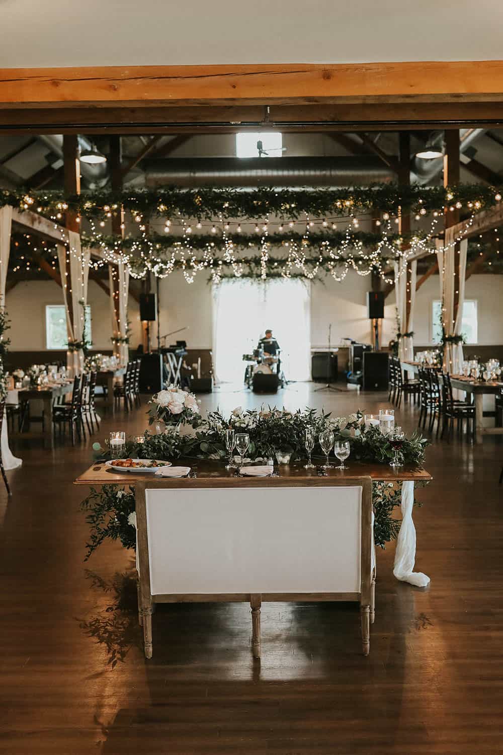 Beautiful wedding reception decorated with string lights, floral arrangements, and elegant table set.